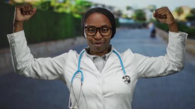 Beyaz önlüklü ve steteskop takmış bir kadın kenar mahallede güven içinde poz veriyor, mesleğinin gücünü ve gururunu gösteriyor..