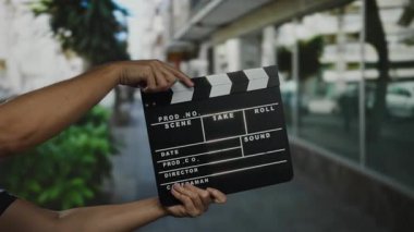 Şehrin sokaklarında film yapımı için el çırpma tahtası tutan adam, şehir ortamında film çekme sürecini gösteriyor, canlı açık hava atmosferini yansıtıyor..