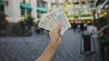 Yoğun bir şehir caddesinde Czech Koruna banknotlarını tutan erkek el, bir şehir ortamında ticaret ve para alışverişini işaret ediyor..
