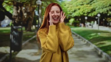 Parlak sarı kazaklı, kızıl saçlı, güneşli bir parkta gülen bir kadın sonbahar güzelliğini ve açık hava güzelliğini gözler önüne seriyor..