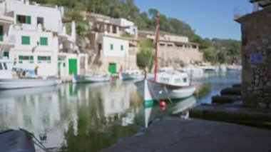Mallorca 'daki Cala figürünün bulanık görüntüsü. Botlar yavaşça yüzüyor, canlı renkler sakin suya yansıyor, güneşli bir Akdeniz liman kasabasının huzurlu özünü yakalıyor..