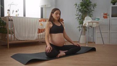 Modern bir yatak odasında yoga yapan hamile bir kadın, doğal ışık ve sakinleştirici dekorla çevrili bir beşiği var. Doğum sırasında rahatlamayı vurguluyor..