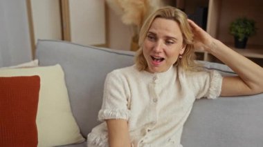 Rahat bir oturma odasında rahat bir kanepede dinlenen, rahat kıyafetler giyen, sıcak renkli yastıkları olan ve sade atmosferi geliştiren, boş zamanların tadını çıkaran bir kadın..