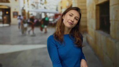 Kadın jestleri, sokak ortasında, açık havada, mavi süveter giyerek, şehir manzarası arka planında, duyguları ifade ederek, canlı sahnede genç beyaz kadın....