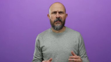 Gri kazaklı kel adam, elleri ile hareket eden, soyutlanmış mor arka plana karşı düşünceli görünüyor..