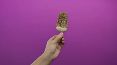 Beyaz adam elinde pembe arka planda çikolatalı dondurma tutuyordu. Tatlı konsepti olarak stüdyo ışıklarında izole edilmiş bir el kullanıyordu.