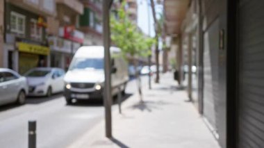 Bulanık cadde sahnesinde açık hava kentsel bir çevrede, görünür vitrinleri ve binaları olan bir minibüs ve çözünmüş arabalar var.