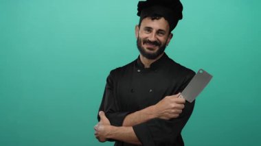 Sakallı İspanyol erkek aşçı canlı yeşil bir arka planda siyah bir üniformayla satırı kavrıyor..