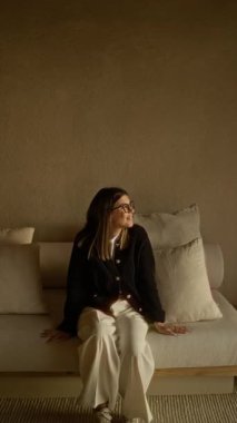 Akdeniz 'de, bej duvar ve yastıklı, gözlük ve süveter takan, doğal ışıkla rahatça gülümseyen bir kadın..