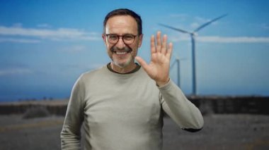 Güneşli bir günde açık bir tarlada gülümseyen ve el sallayan olgun İspanyol bir adam..