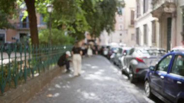 Roma caddesinde yürüyen insanlar, park etmiş arabalar ve yeşil yapraklar, İtalyan eski kasabasındaki günlük hayatın özünü yansıtıyor..