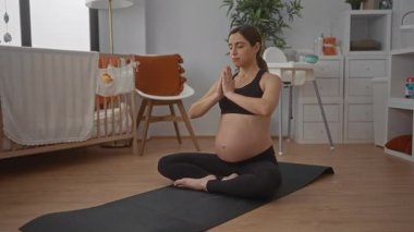 Hamile kadın, huzurlu bir yatak odasında beşikle yoga yapıyor, spor kıyafeti giyiyor, sakin ve sağlıklı bir yaşam tarzı sergiliyor..