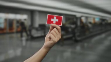 Kapalı havalimanı terminalinde arkaplanı bulanık İsviçre bayrağı taşıyan adam..