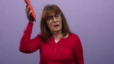 Kırmızı gömlekli son sınıf öğrencisi kadın, mor arka planda kafasına buz torbası dayamış. Ayrı bir ortamda rahatsızlık ya da baş ağrısı gösteriyor..