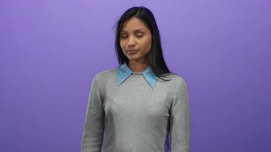 Gri kazaklı genç İspanyol kadın canlı mor bir arka plana karşı ciddi bir şekilde alkış tutuyor, izole bir ortamda, duygu ve ifade gösteriyor..