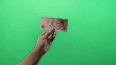 İzole edilmiş yeşil arka plan duvarına karşı elinde Türk lirası banknot tutan adam merkez bankasının parasıyla mali işlem kavramını resmediyor..