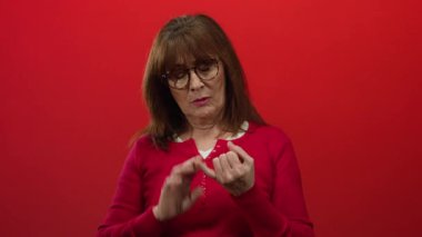 Gözlüklü yaşlı İspanyol kadın parmaklarını kırmızı duvarlara yaslıyor. Kırmızı bir süveter giyiyor, odaklanıyor ve konsantre oluyor..