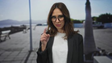 Açık gökyüzü ve okyanus manzaralı güneşli bir sahil geçidinde, gözlüklü ve rahat bir sahil atmosferi sergiliyor..