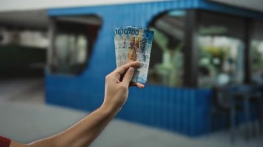 Elinde İsviçre frangı banknotları tutan bir adam var. Şehir caddesinde arka planda mavi bir bina var. Hafif ışıklandırma altında..