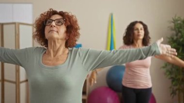 Spor salonunda yoga yapan kadınlar, senkronize pozlarla konsantrasyon ve denge gösterisi yapan, fitness ekipmanları ve davetkar bir atmosferle çevrili kadınlar..
