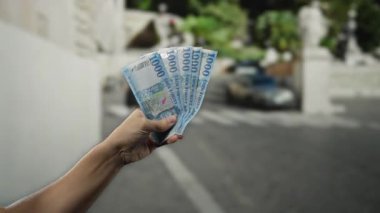 Bir şehir caddesinde elinde Macar banknotları tutan adam odaklanmış ön planı ve bulanık şehir geçmişiyle finans ve ekonominin özünü yakalıyor..