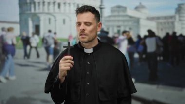 Pisa kulesinin önünde haç tutan rahip güneşli bir günde insanlarla çevrili. İkonik italyan şehrinde ruhani bağlılığı yakalıyor.