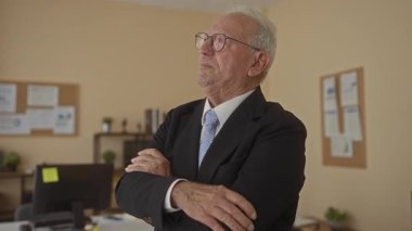 Takım elbiseli kıdemli bir adam düşünceli bir şekilde ofis ortamında duruyor, çizelgeler ve bitkiler profesyonel iç mekan düzenini geliştiriyor..