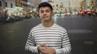 Genç adam hareketli şehir caddesinde sıradan çizgili gömleğiyle, canlı şehir gece lambalarıyla çevrili duruyor.