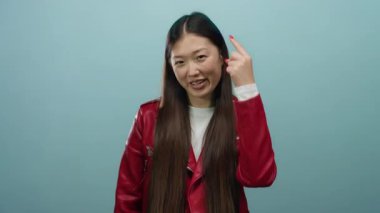 Kırmızı ceketli, mavi arka planda gülümseyen bir kadın güven ve neşeyle barış işareti gösteriyor..