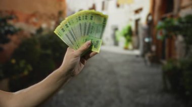 Bangladeş banknotlarını elinde tutan adam, bir şehir caddesinde para sergiliyor, açık hava ortamında finansal refah ve para birimini temsil ediyor..