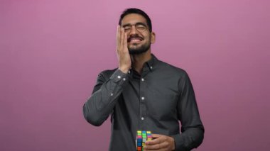 Elinde küple pembe arka planda gülümseyen, gözlüklü, siyah gömlekli, mutluluğu ve tefekküre dalmayı ifade eden genç bir adam..