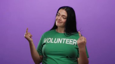 Yeşil gönüllü gömlekli genç, iri yarı bir kadın, iki elini de canlı mor bir arka plana karşı kullanarak cesur bir jest yapıyor, asi tavır ve kendine güvenini gösteriyor..