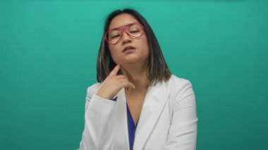 Gözlüklü ve beyaz ceketli kendine güvenen genç bir kadın izole edilmiş yeşil duvar arkaplanına karşı poz veriyor, profesyonellik ve modernlik yayıyor ve sakin bir ifadeyle..