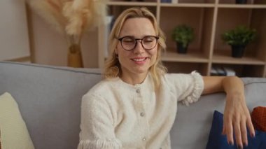 Modern bir oturma odasında rahat bir kanepede dinlenen bir kadın, rahat bir yaşam tarzı sergiliyor sarı saçlar ve gözlüklerle evde rahat bir şekilde otururken.