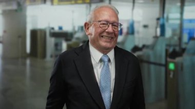 Havalimanında kapalı alanda duran, modern bir terminal ortamında gelişigüzel etkileşim kurarken seyahat düzenini ve profesyonel davranışları tasvir eden iş adamı..