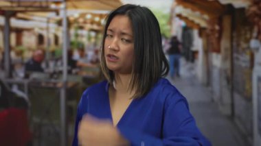 Mavi bluzlu genç bir kadın şehir merkezindeki hareketli bir teras restoranına dik dik bakıyor..