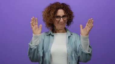 Orta yaşlı İspanyol bir kadın, elleri mor bir duvarın önünde, gözlük ve kot gömlek giyer ve büyük beden bir konsept taşır..