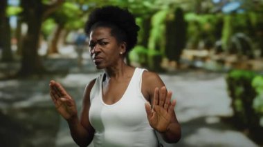 Huzurlu bir parkta, yemyeşil ağaçların gölgesinde duran bir kadın..