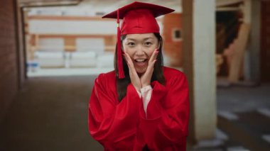 İnşaat alanındaki mezuniyeti kutlayan kırmızı başlık ve cübbe giyen bir kadın beklenmedik bir ortamda heyecan ve başarıyla neşeli bir anı yakalıyor..