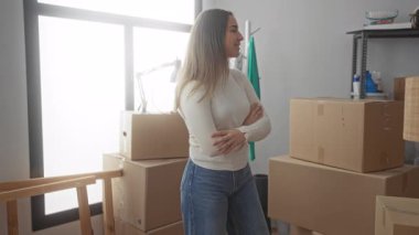 Yeni evdeki kutuları açan kadın, etrafı karton kaplarla çevrili iken gülümseyen ve düzenleyen kadın, büyük pencereden içeri giren güneş ışığı, rahat bir atmosfer yaratıyor..