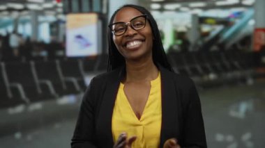 Havaalanı terminalinde gözlüklü, sarı tişörtlü ve siyah ceketli bir kadın hareketli bir ruh hali ve hareketli bir evin içinde seyahat beklentisi yakalıyor..