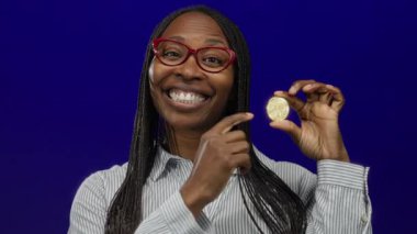 Elinde kripto para tutan kadın, izole edilmiş mavi arka plana parlak bir şekilde gülümsüyor, engelleme teknolojisi ve finansal yenilikler üzerine odaklanmış sanal para birimi kavramı sergiliyor..