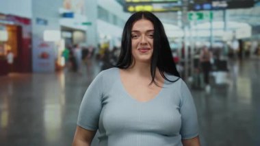 Kapalı bir havaalanı terminalinde gülümseyen genç bir kadın dünya çapında seyahat ve modern seyahat deneyimleri sergiliyor