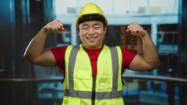 Güvenli yelek ve kask giyen genç adam modern inşaat alanında kaslarını rahatça esnetiyor..