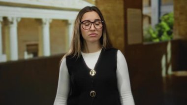 Genç bir kadın, klasik mimarisi olan, gözlük takan ve siyah yelek giyen, yön tarifi öneren ya da bilgi sunan bir açık hava üniversitesine bakıyor..