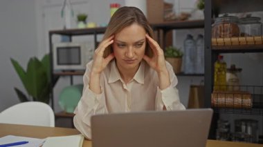 Kadın, çevresi bitki ve raflarla çevrili modern ofis ortamında dizüstü bilgisayarla çalışırken, kapalı alanda yoğun bir ortamda hayal kırıklığı ve konsantrasyon taşıdığını vurguladı.