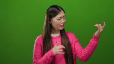 Gitar çalan kadın, canlı yeşil arka plana karşı pembe süveter giyerek güven içinde poz veriyor ve neşe ve yaratıcılığı yakalıyor.