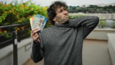 Açık havada elinde İsviçre frangı banknotları olan ve boynu ağrıyan bir adam, canlı bir şehir bahçesine karşı kurulmuş, rahatsızlık ve zenginliğin karmaşık bir ifadesini yakalıyor..