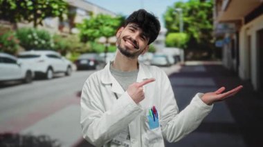 Beyaz önlüklü bir adam gülümsüyor ve arka planda ağaçlar ve park edilmiş arabalar olan bir şehir caddesini işaret ediyor..