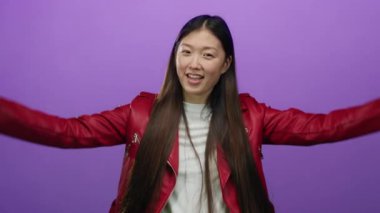 Kırmızı ceketli bir kadın mor bir arka planda neşeli bir şekilde dans ediyor. Kollarını kaldırarak ve dalgalı saçlarıyla mutluluk ve enerji saçıyor..